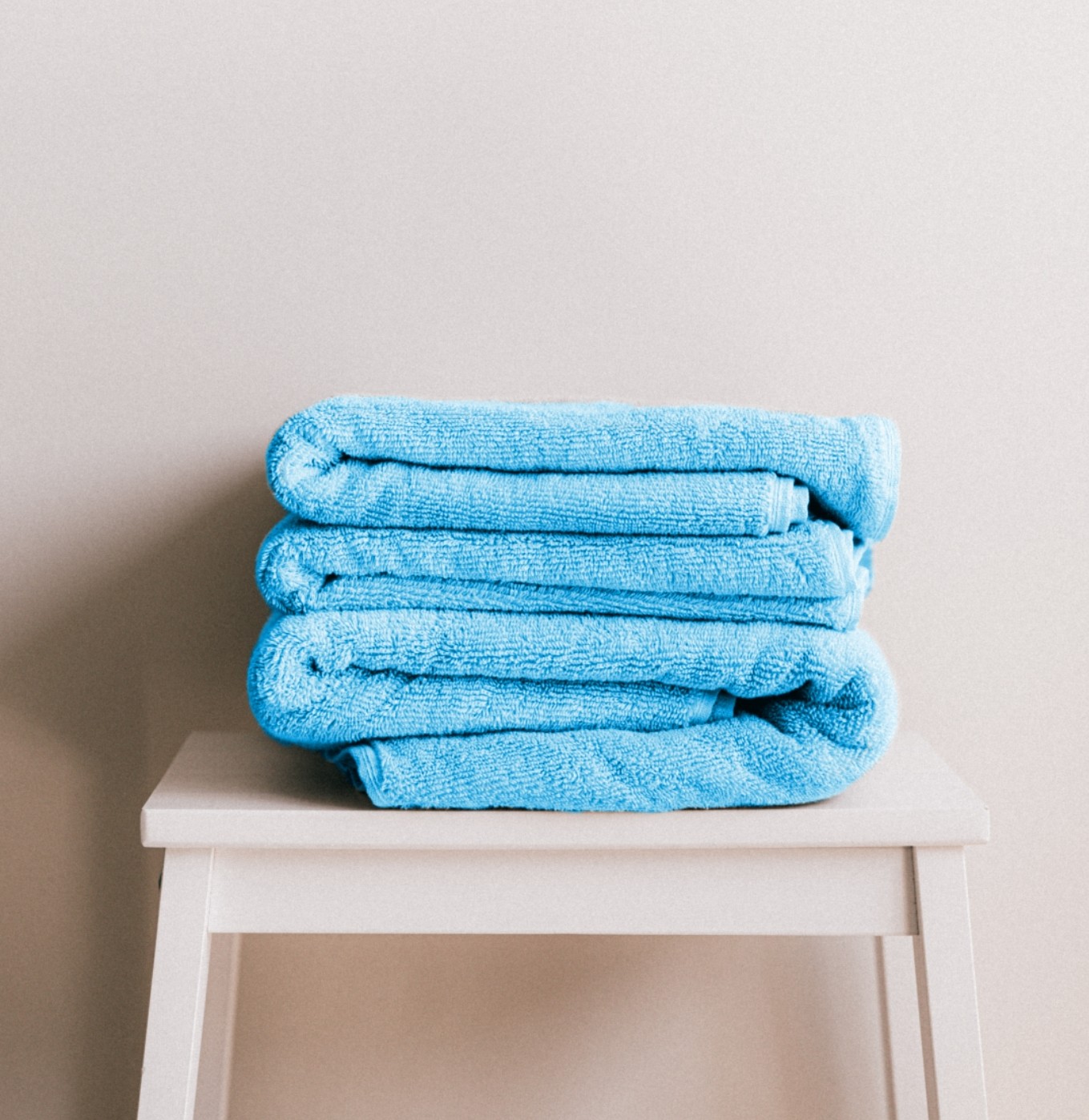 supreme aqua 2 hand towels stacked ontop of each other on a wooden stool